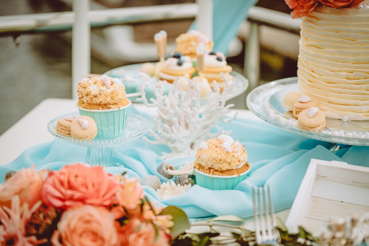 Ein Tisch mit Cupcakes und Blumen auf einer blauen Tischdecke.