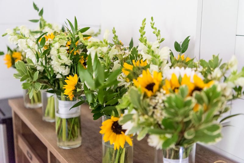 Sonnenblumen und weiße Blumen in Vasen auf einem Holztisch.