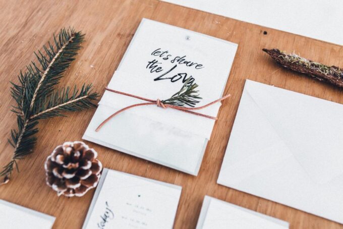 Hochzeitseinladungen mit Tannenzapfen und Tannennadeln auf einem Holztisch.