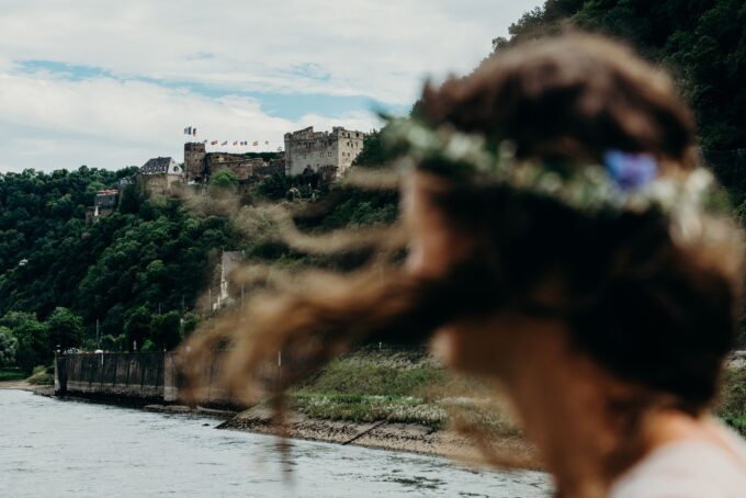 Eine Braut mit Blumenkranz vor einem Schloss am Rhein.