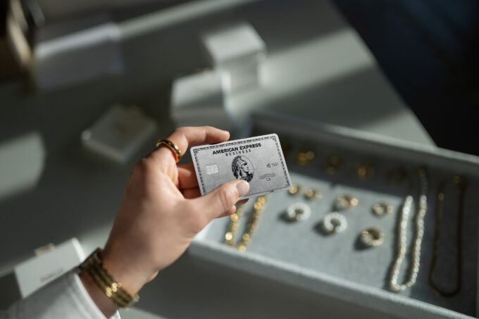 Die Hand einer Person hält im Sonnenlicht eine American-Express-Kreditkarte über ein Schmucktablett mit verschiedenen Schmuckstücken.