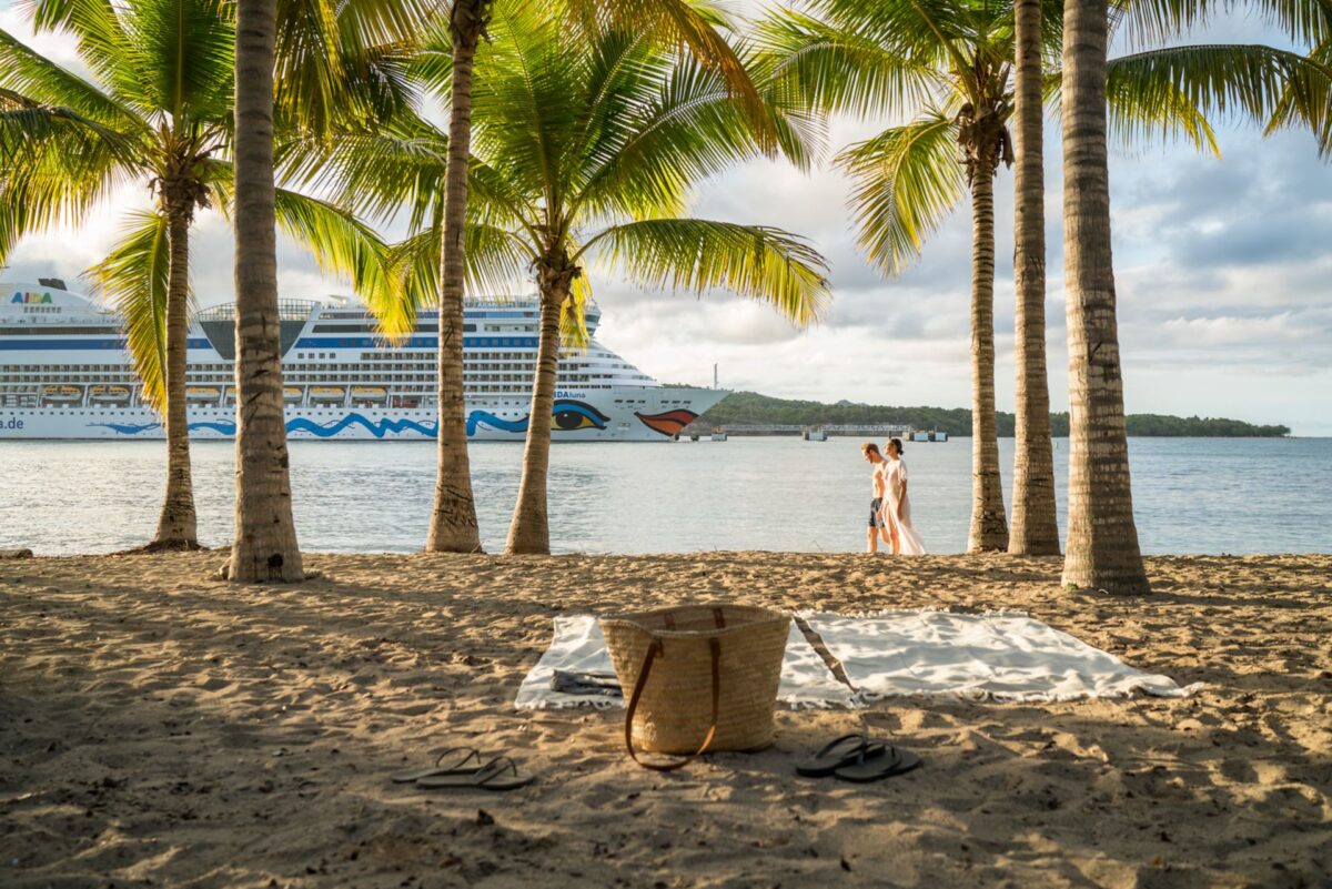 Ein Paar geht gemeinsam am Strand entlang. Im Hintergrund sieht man die AIDA.