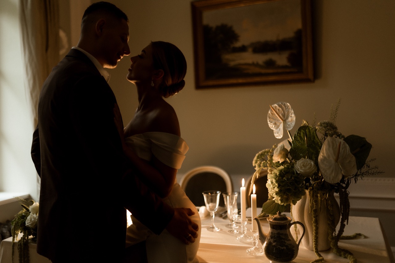 Das Brautpaar küsst sich vor einem Hochzeitstisch im Schloss Manowce.