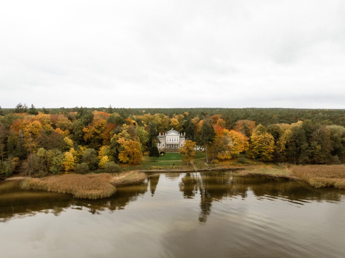 Schloss Manowce mit gepflegten Rasenflächen und einem romantischen Ausblick auf einen nahegelegenen See.