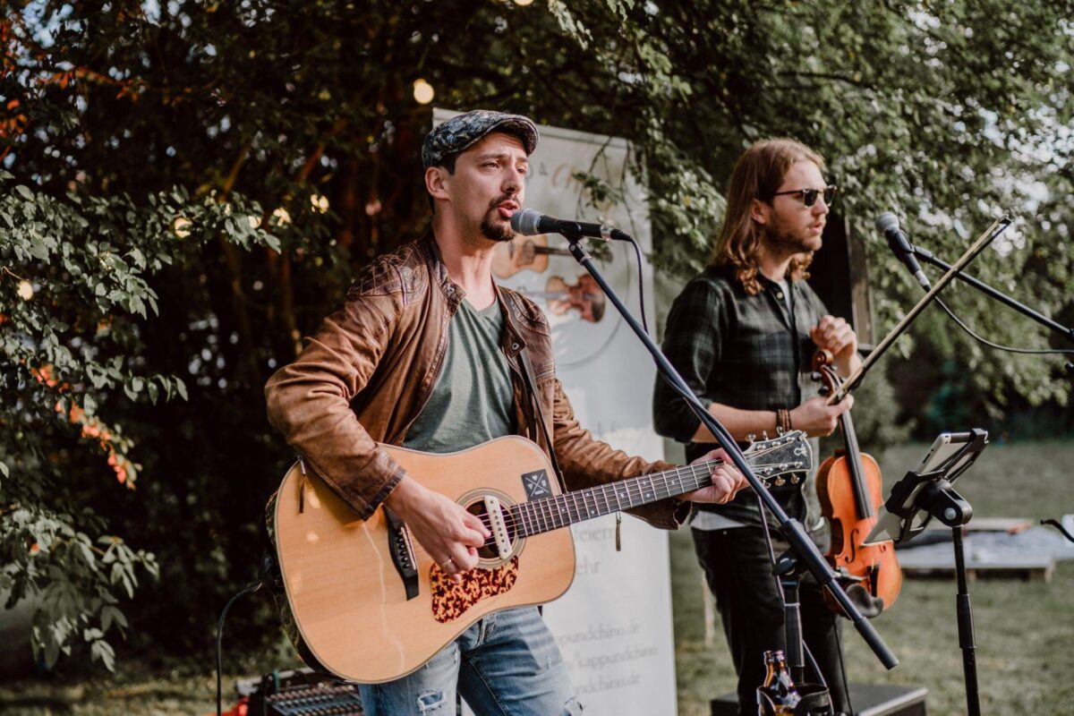 Zwei Männer singen und spielen eine Akustikgitarre.